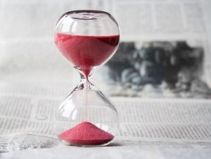Hourglass with running red sand on an open newspaper